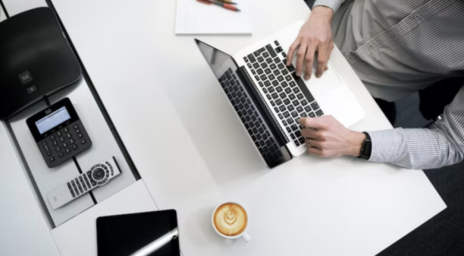 Persona usando portátil sobre mesa de madera blanca.